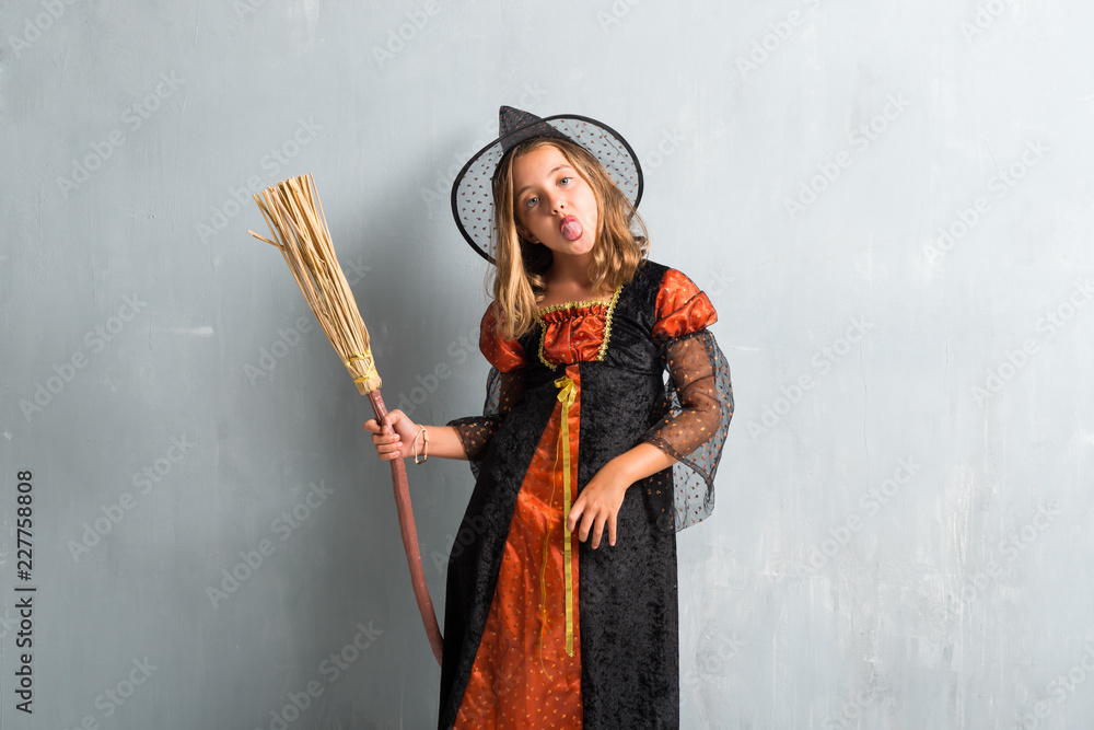 Little girl dressed as a witch and holding a broom for halloween holidays taking out her tongue