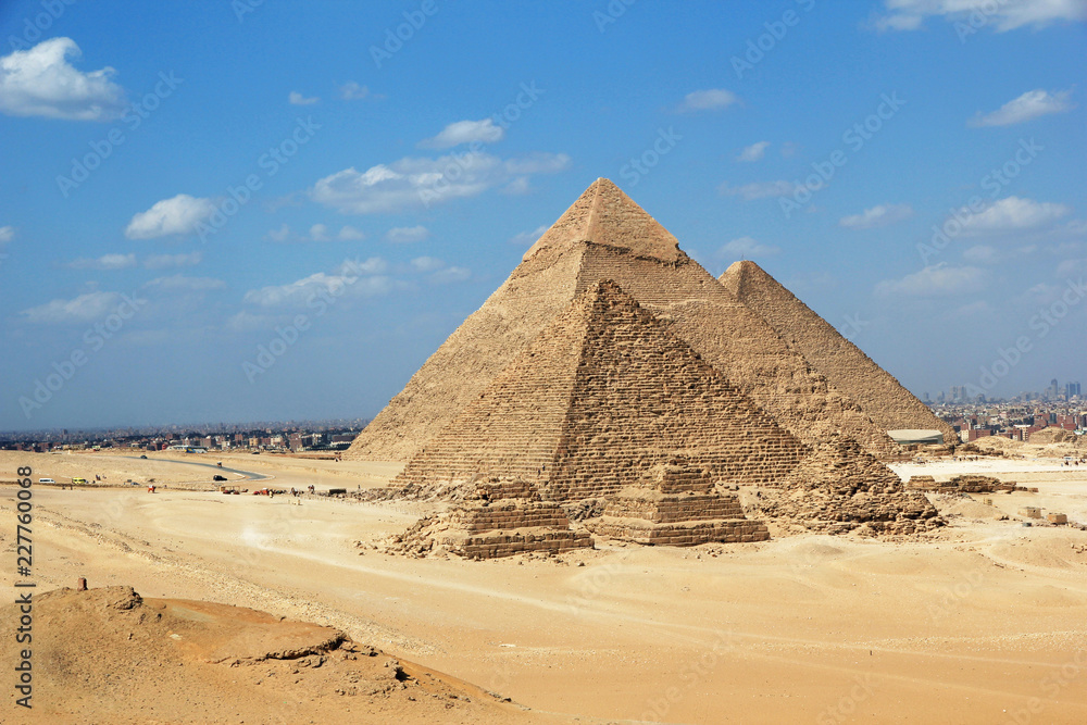 Great Pyramids of Giza set against a bright blue sky and golden yellow desert sands but with the encroaching city of Cairo in the background Great Pyramids of Giza set against a bright blue sky and golden yellow desert sands but with the encroaching city of Cairo in the background