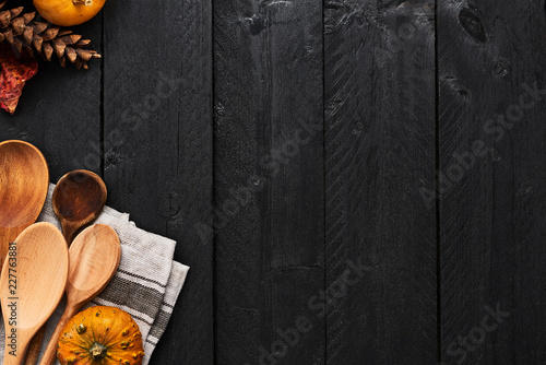 Autumn vegetables cooking preparation. Top view of pumpkins, wooden spoons and dishtowel on black wooden background with copy space.