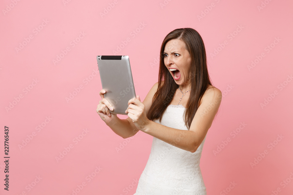 Irritated angry bride woman in wedding dress screaming swearing working on tablet computer making video call isolated on pink background. Wedding to do list. Organization of celebration. Copy space. Irritated angry bride woman in wedding dress screaming swearing working on tablet computer making video call isolated on pink background. Wedding to do list. Organization of celebration. Copy space.
