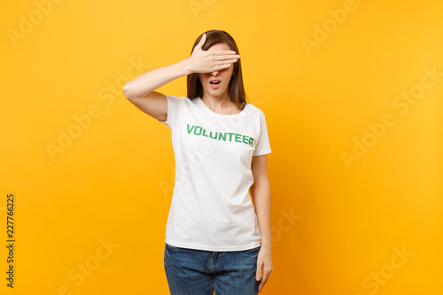 Portrait of sad upset shocked young woman in white t-shirt with written inscription green title volunteer isolated on yellow background. Voluntary free assistance help, charity grace work concept.