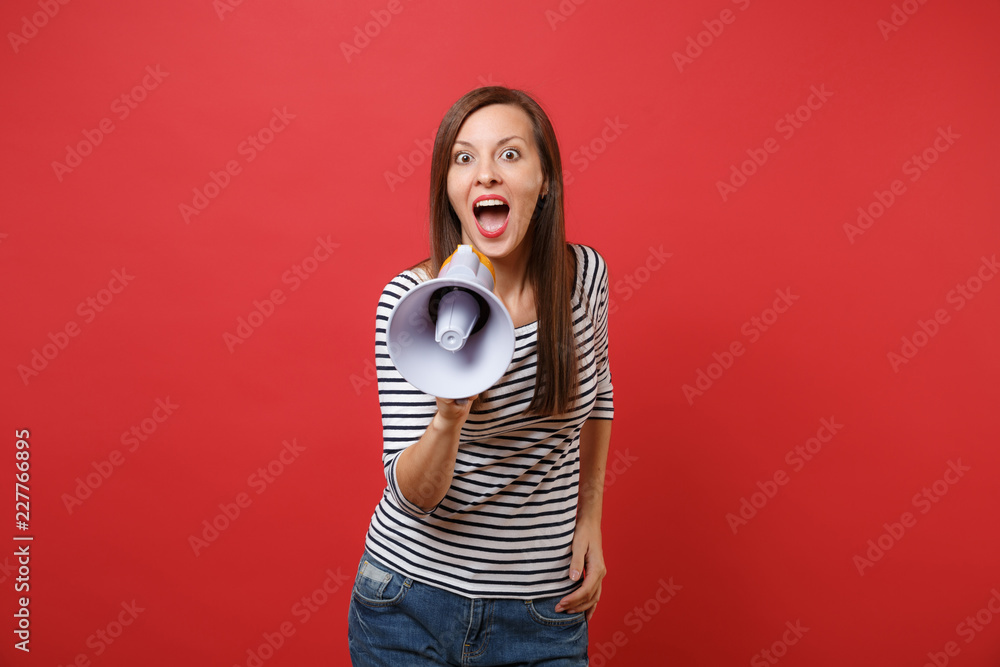 Excited young woman in striped clothes screaming on megaphone keeping mouth wide open looking surprised isolated on red wall background. People sincere emotions, lifestyle concept. Mock up copy space. Excited young woman in striped clothes screaming on megaphone keeping mouth wide open looking surprised isolated on red wall background. People sincere emotions, lifestyle concept. Mock up copy space.