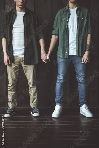 Very special bond. Cropped portrait of two young guys holding hands while standing on wooden background