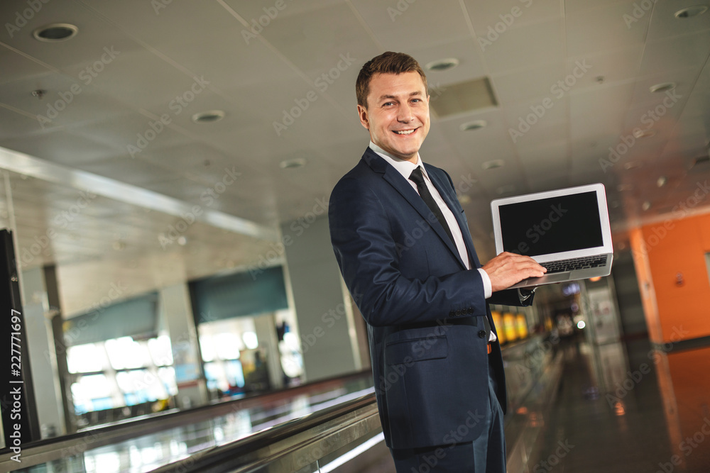 Waist up portrait of blithesome businessman holding laptop and looking at camera with wide smile Waist up portrait of blithesome businessman holding laptop and looking at camera with wide smile