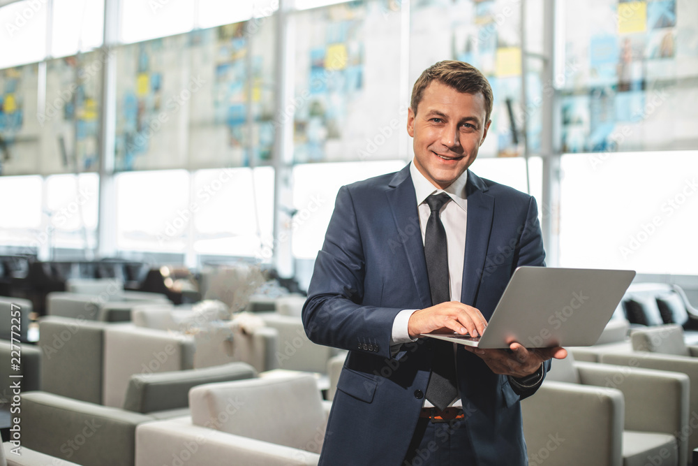Waist up portrait of cheerful businessman standing in cafe and typing on device. Copy space on left side Waist up portrait of cheerful businessman standing in cafe and typing on device. Copy space on left side