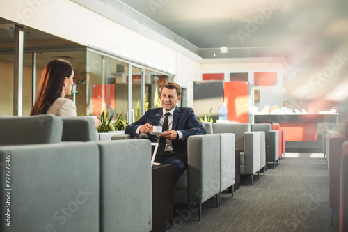 Businessman having cup of beverage and looking at female partner with smile. Copy space on right side