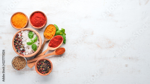 Fototapeta Naklejka Na Ścianę i Meble -  A set of Spices and herbs on a white wooden table. Basil, pepper, saffron, spices. Indian traditional cuisine. Top view. Free copy space.