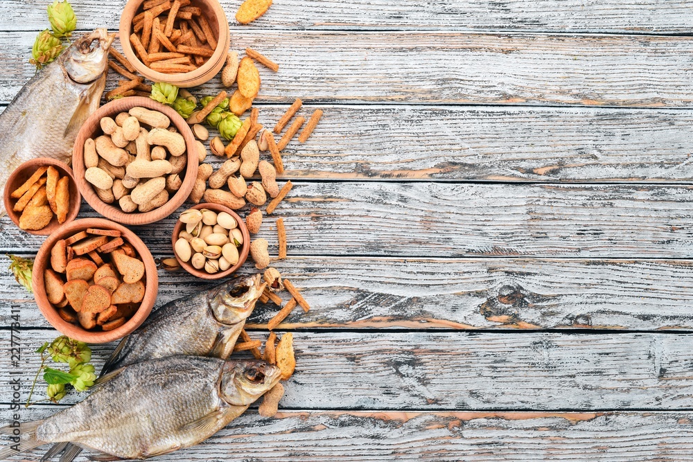 Snacks for beer. Salted crackers, Dried Fish, Chips, Nuts, Peanuts, Pistachios. On a wooden background. Free space for text. Top view. Snacks for beer. Salted crackers, Dried Fish, Chips, Nuts, Peanuts, Pistachios. On a wooden background. Free space for text. Top view.