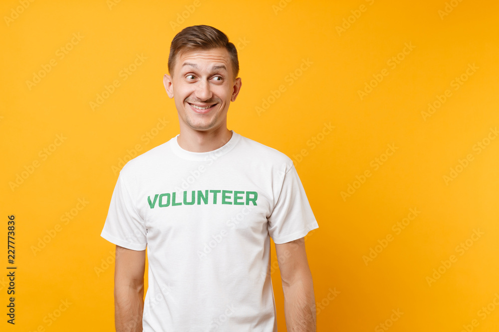 Portrait of happy smiling satisfied young man in white t-shirt with written inscription green title volunteer isolated on yellow background. Voluntary free assistance help, charity grace work concept. Portrait of happy smiling satisfied young man in white t-shirt with written inscription green title volunteer isolated on yellow background. Voluntary free assistance help, charity grace work concept.