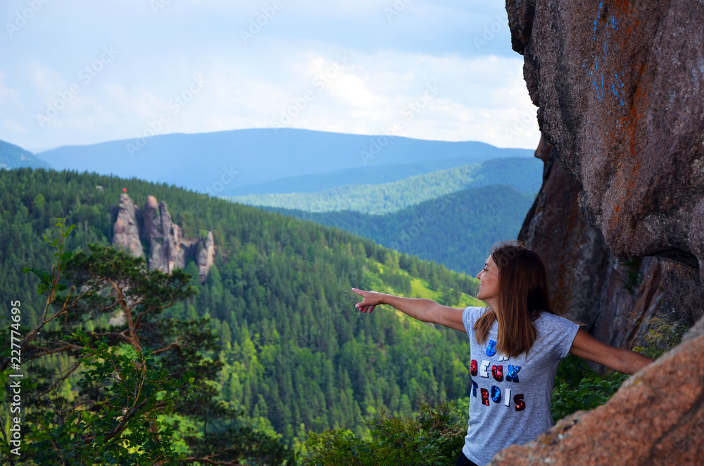Naklejka premium A girl stands on a high rock on the edge of the cliff. Beautiful autumn forest. Autumn in the mountains. The girl looks dreamily into the distance. Unity with nature. Beautiful view from the top.