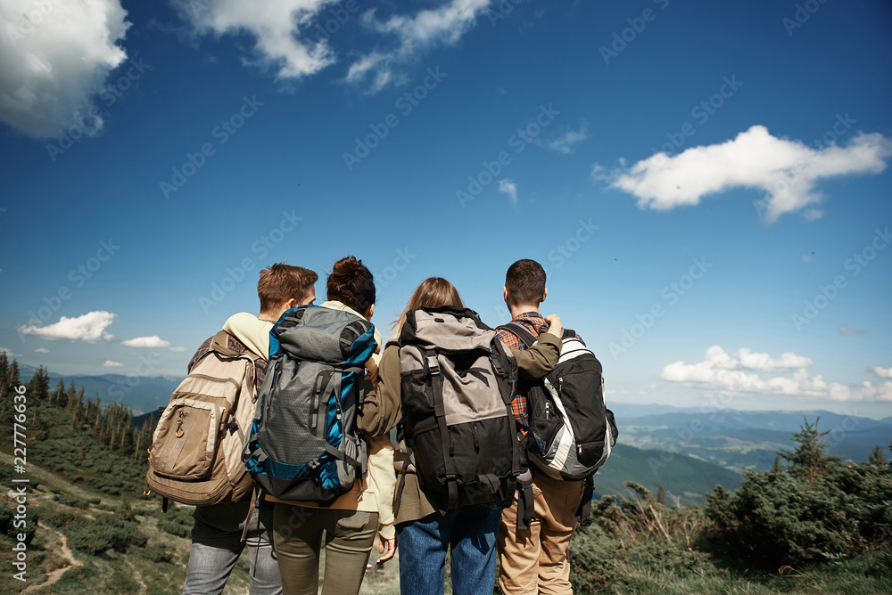 Two women and two men standing on peak with focus on back and looking forward. They enjoying marvelous landscapes downhill Two women and two men standing on peak with focus on back and looking forward. They enjoying marvelous landscapes downhill