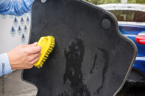 The hand of the person cleans an automobile rug.