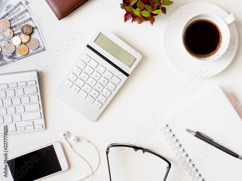 top view of accounting concept with keyboard, smartphone, notebook, coffee cup, calculator and money on white table background.