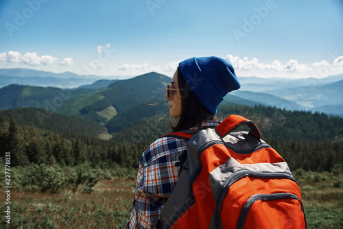 Tranquil woman is standing with rucksack while wearing sunglasses. She is hiking and enjoying view of high peaks and nature around female backpacker is spending time in mountains