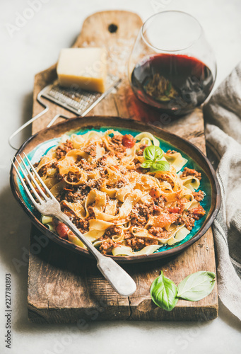 Italian traditional pasta dinner. Tagliatelle bolognese with minced meat, tomato sauce and parmesan cheese and glass of red wine over rustic wooden board, selective focus photo