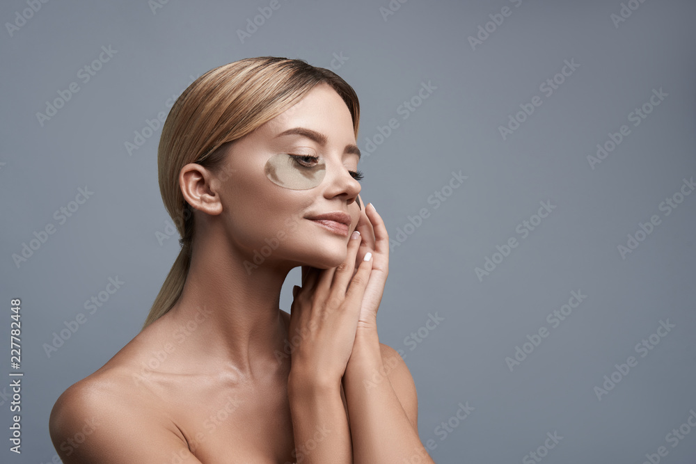 Portrait of the young lady sitting against the grey background with eye patches and smiling happily Portrait of the young lady sitting against the grey background with eye patches and smiling happily