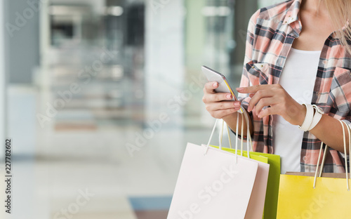 Woman in casual using smartphone and holding colourful bags