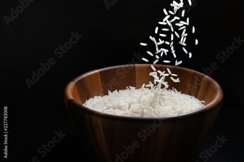 Pouring jasmine rice into a wooden bowl on black background