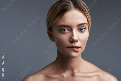 Biting the lip. Cute young woman standing against the grey background and thoughtfully biting her lip while looking at you