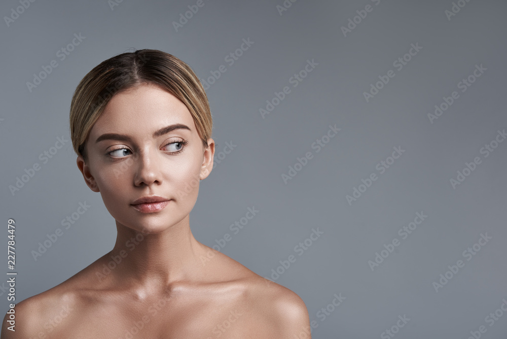Curiosity. Lovely young lady slightly smiling and feeling curious while standing against the grey background and looking to the left Curiosity. Lovely young lady slightly smiling and feeling curious while standing against the grey background and looking to the left