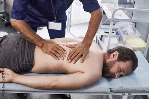 Doctor making massage to male patient while showing correct technique for performing treatment photo