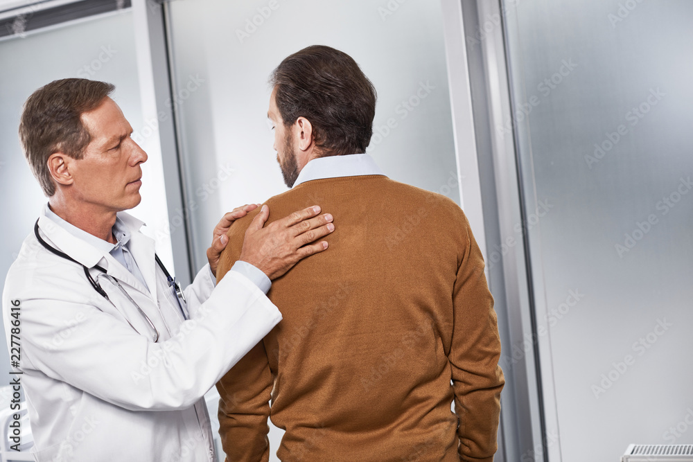 Waist up portrait of adult specialist examining shoulder joint of his patient in medical room Waist up portrait of adult specialist examining shoulder joint of his patient in medical room