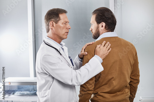 Adult medical adviser exploring possible reason of pain in upper spine of his male patient