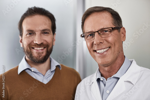 Portrait of adult doctor and male patient staying in clinic during examination and smiling