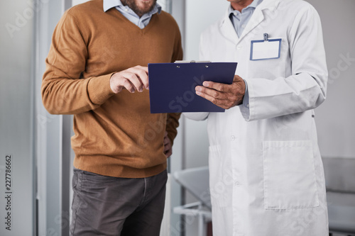 Doctor in white coat showing medical documents for patient and discussing his diagnosis