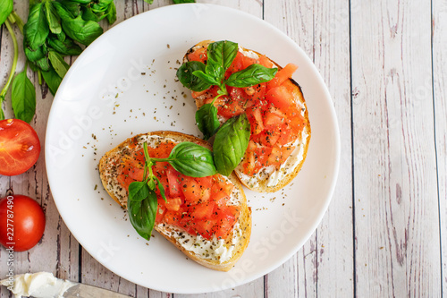 Traditional toasted Italian tomato bruschetta with spice and basil on light wooden background. Top view vith copy space photo