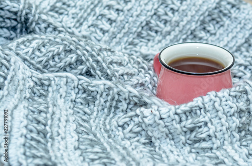 Cup of hot tea dressed in knitted warm winter scarf or warm knitted sweater. Still life of a scarf and cup of tea. Winter, autumn time. Cozy and soft winter background.