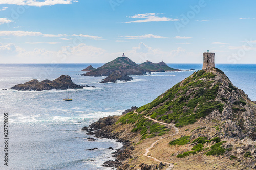 View of Pointe de la Parata on the west coast of Corsica. A ruined Genoese tower sits on top of the rocky promontory overlooking the archipelago of the Sanguinaires and a sailing boat on a sunny day.