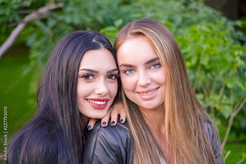 Girlfriend girls in the Park on the background of green bushes and lawn. Two girls in the park Girlfriend girls in the Park on the background of green bushes and lawn. Two girls in the park