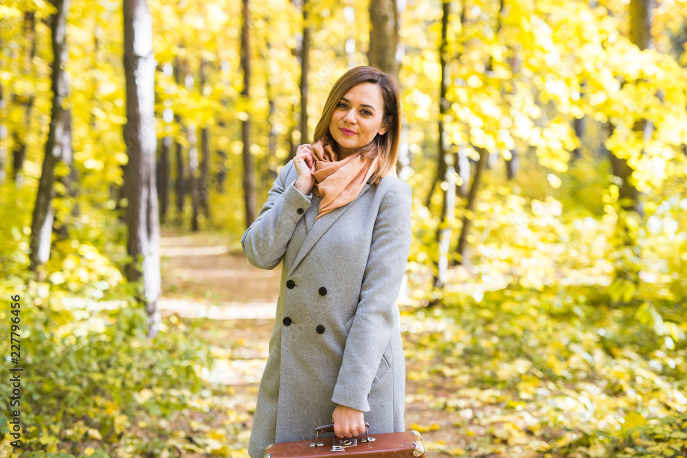 fashion, season and people concept - happy young woman is going on a trip with retro suitcase on a background of autumn foliage