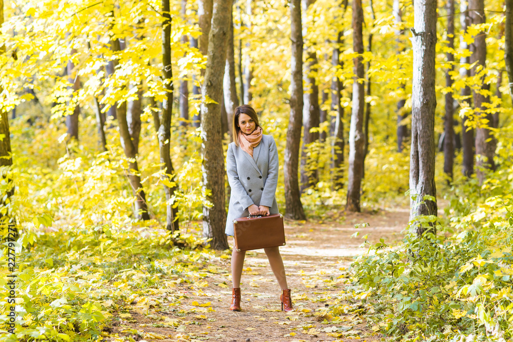 Fall, season and people concept - young woman standing with retro suitcase in autumn park Fall, season and people concept - young woman standing with retro suitcase in autumn park