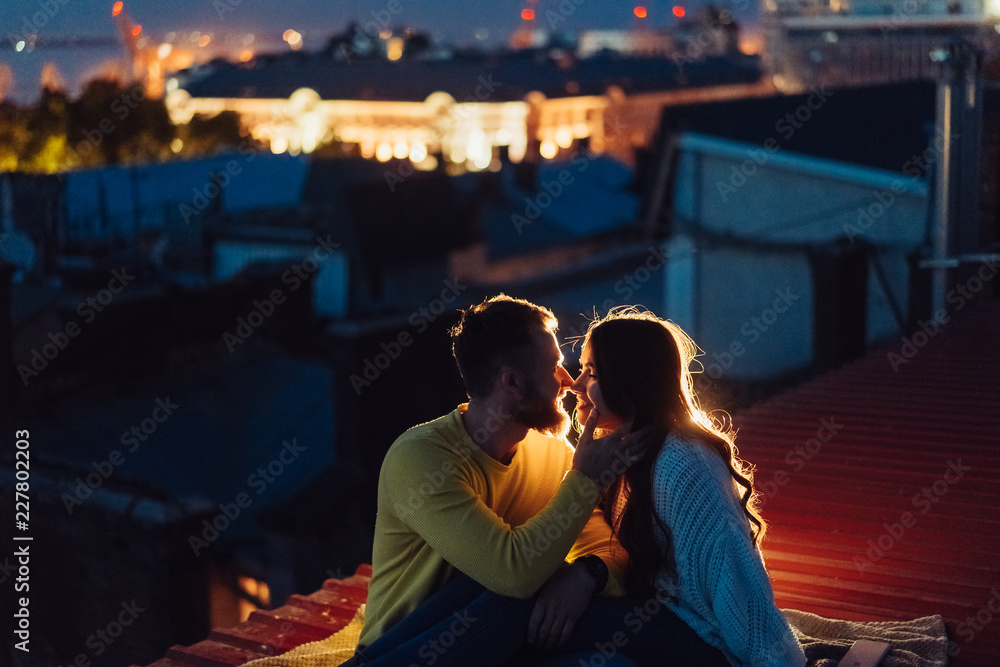 Loving couple is sitting on the roof of the house. Beautiful evening