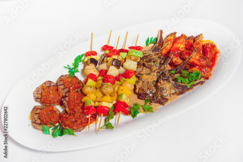 Vegetable skewers with meat on a white plate. Baked vegetables on shashkah with beef. Grilled meat on a barbecue with vegetables photo