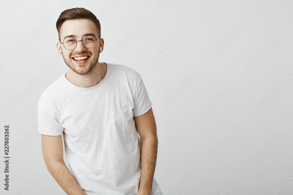 Portrait of happy friendly-looking stylish caucasian guy in glasses and wireless earphones laughing and smiling broadly squinting at camera from delight and positive emotions listening favorite music Portrait of happy friendly-looking stylish caucasian guy in glasses and wireless earphones laughing and smiling broadly squinting at camera from delight and positive emotions listening favorite music