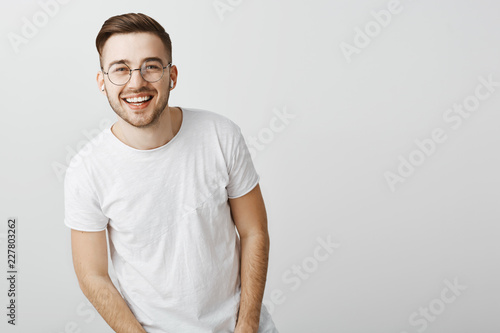 Portrait of happy friendly-looking stylish caucasian guy in glasses and wireless earphones laughing and smiling broadly squinting at camera from delight and positive emotions listening favorite music © Cookie Studio