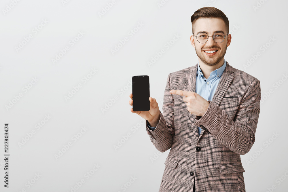 Making money easier with this app. Portrait of pleased carefree stylish male entrepreneur in glasses and formal jacket holding smartphone pointing at phone screen with delighted friendly smile Making money easier with this app. Portrait of pleased carefree stylish male entrepreneur in glasses and formal jacket holding smartphone pointing at phone screen with delighted friendly smile