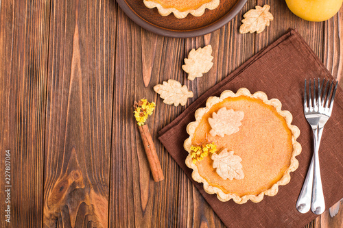 Pumpkin pie with cinnamon and cookies on brown napkins on wooden background with autumn yellow leaves.