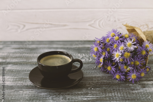 Romantic background with a cup of coffee, a bouquet of purple flowers in craft paper on a gray wooden table