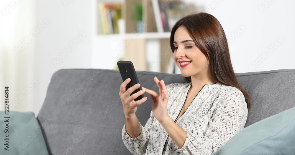 Happy woman browsing smart phone content sitting on a couch at home Happy woman browsing smart phone content sitting on a couch at home