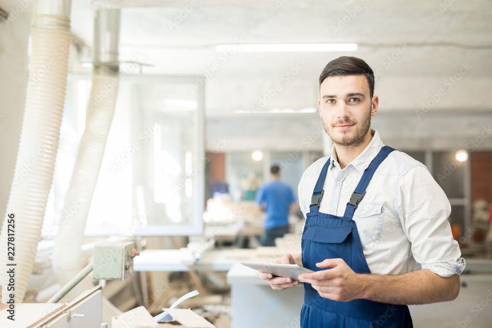 Young worker in overalls looking at you while networking or looking through online data Young worker in overalls looking at you while networking or looking through online data