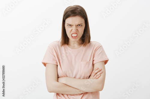 Hate, anger and negative emotions concept. Portrait of outraged and pissed woman, clenching fist grimacing from disdain, frowning eyebrows, looking from under forehead, holding hands crossed on chest