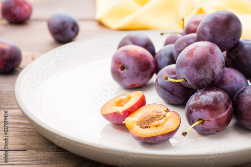 Close-up of a broken ripe blue plum and whole berries on a plate on a wooden table