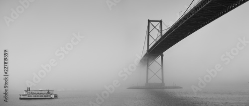 Ferry boat crossing under a suspension bridge in Halifax, Nova Scotia in thick fog. 