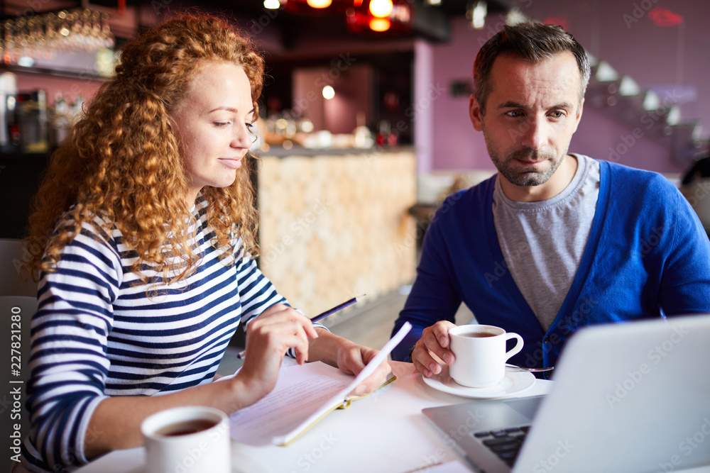 Two young casual colleagues sitting in cafe in front of laptop and working over project Two young casual colleagues sitting in cafe in front of laptop and working over project