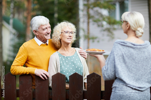 Mature woman giving her new neighbours homemade fresh apple pie on plate over fence photo