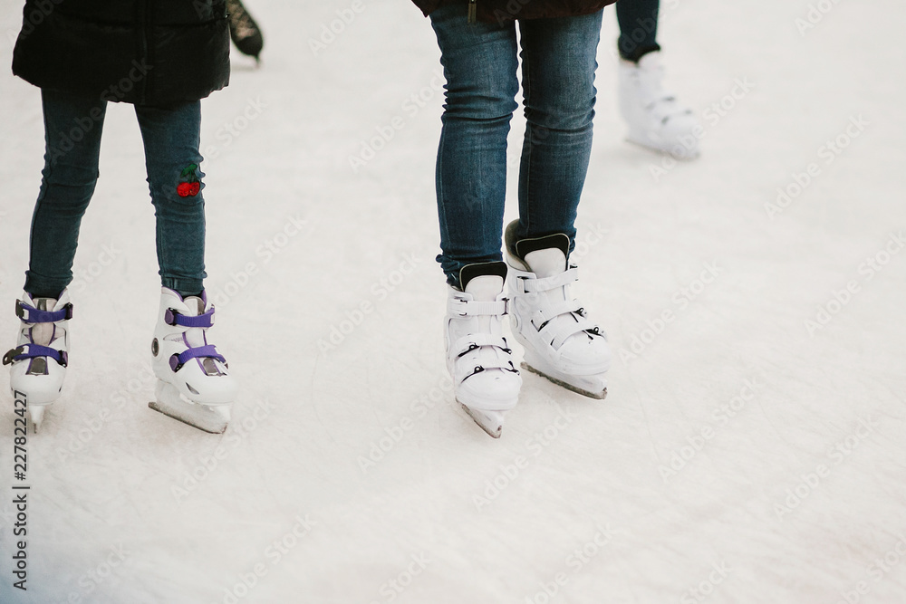 Skaters skating on iceskating ring in european city center in winter holidays. Kids playing on white ice skating ring, healthy activity. Child legs in white skates Skaters skating on iceskating ring in european city center in winter holidays. Kids playing on white ice skating ring, healthy activity. Child legs in white skates